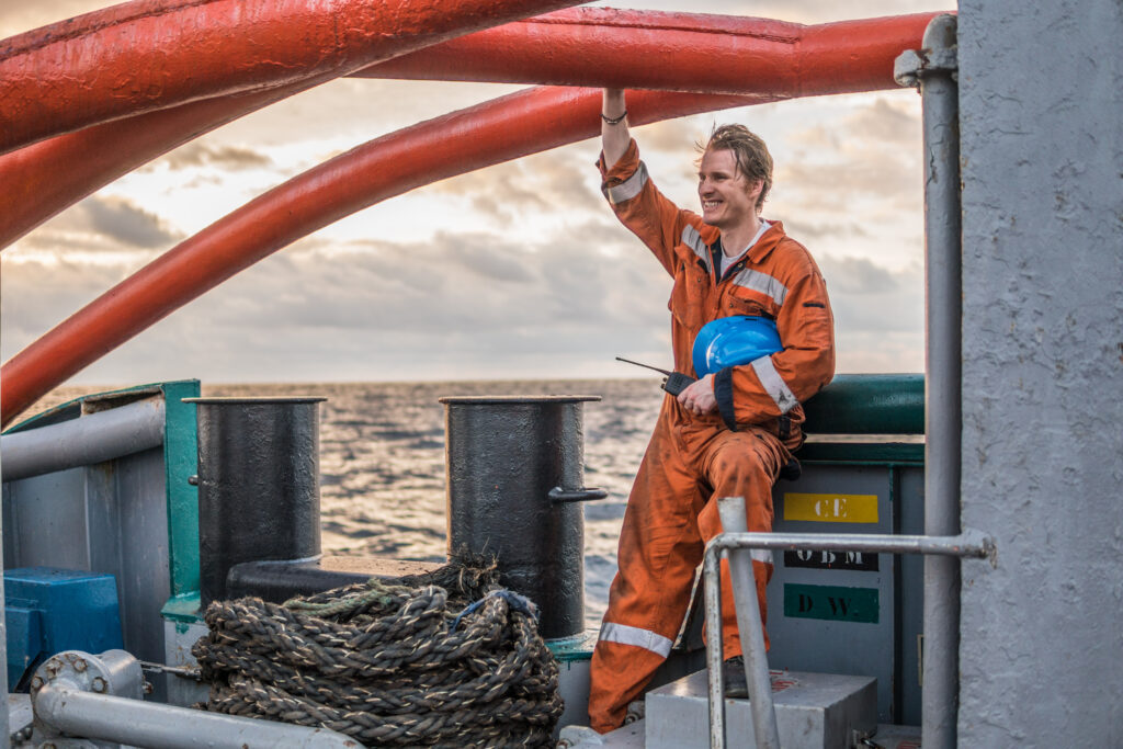 Marine Deck Officer or Chief mate on deck of offshore vessel or ship , wearing PPE personal protective equipment - helmet, coverall. He is smiling